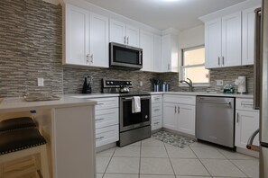 Una cocina moderna con gabinetes blancos, electrodomésticos de acero inoxidable, microondas, horno y lavavajillas.