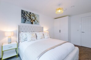 A bedroom with a bed, nightstand, lamp, wardrobe, and a painting on the wall. - 2BDR | Free Parking | Stylish Liverpool Apartment (Liverpool)