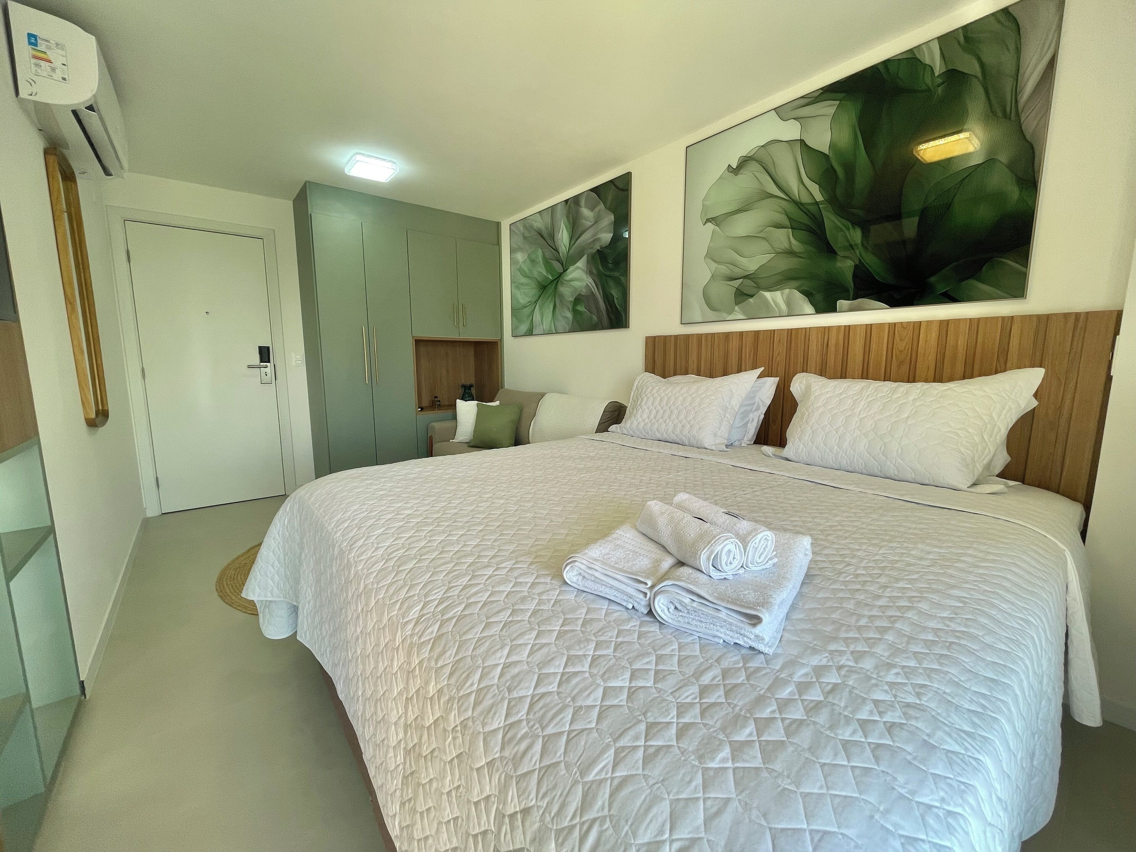 A hotel room with a large bed, a wooden headboard, and two wall-mounted air conditioning units.