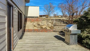 Una terraza de madera que lleva a una casa con un muro de piedra y una parrilla.
