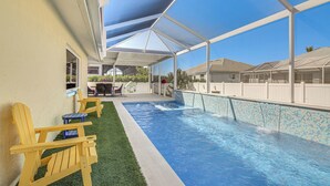 Ein überdachter Swimmingpool mit klarem, blauem Wasser, umgeben von einem weißen Zaun und einer überdachten Veranda mit Adirondack-Stühlen.