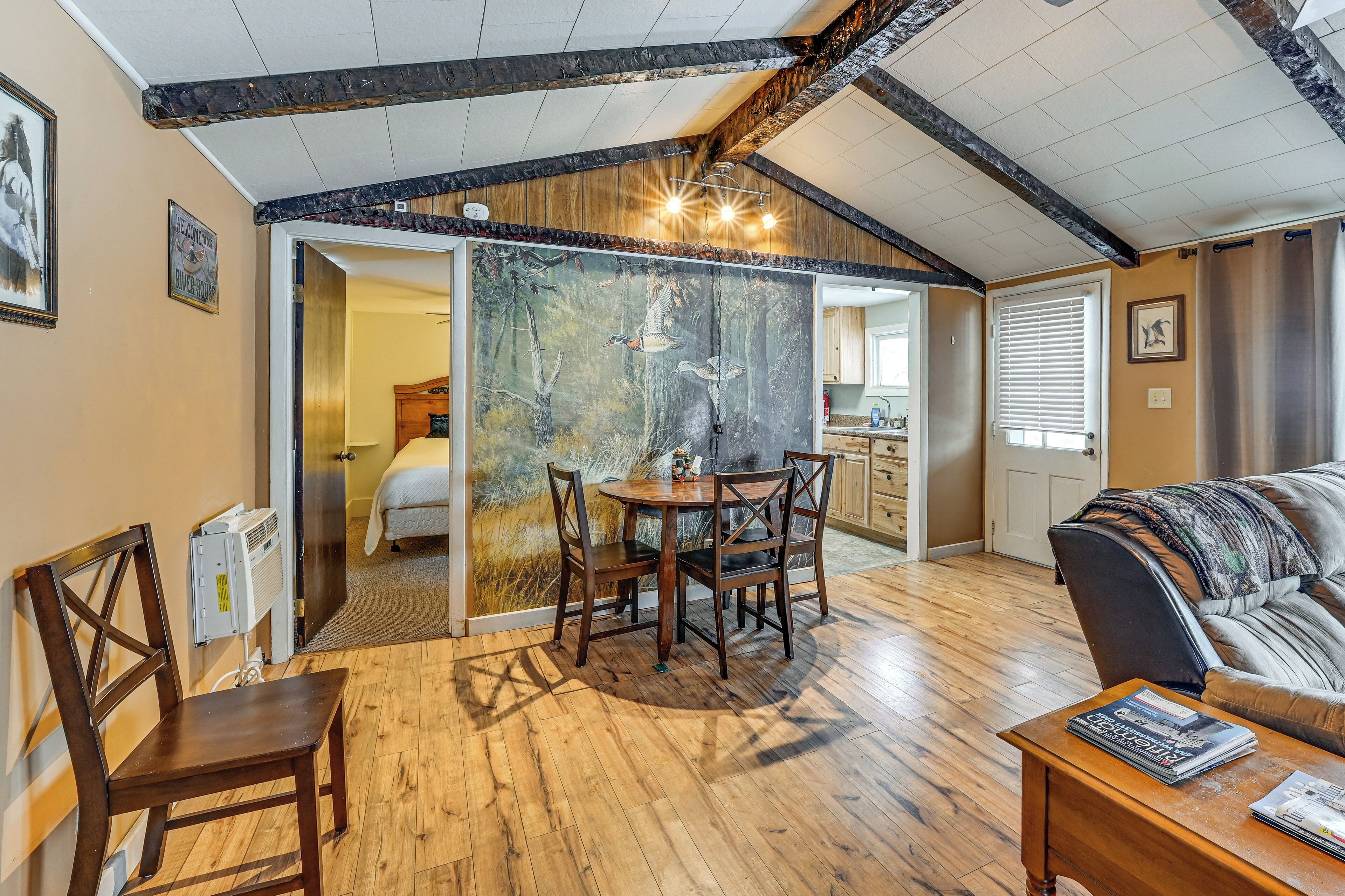 A cozy room with a wooden dining table, a sofa, and a view of a bedroom through a glass door.