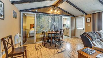 A cozy room with a wooden dining table, a sofa, and a view of a bedroom through a glass door.