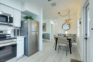 Een moderne keuken met roestvrijstalen apparatuur, een eethoek met rieten stoelen en een decoratieve wand met een bloemendesign.