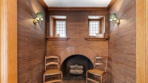 Una habitación con chimenea de ladrillo, dos sillas de madera y dos lámparas de pared.