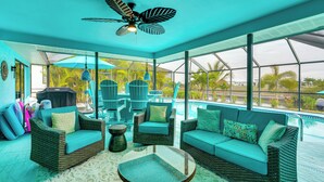 A covered outdoor seating area with wicker furniture, a ceiling fan, and a view of a pool and palm trees. - Family Fun in Cape Coral! Colorful Home w/ Dock (Cape Coral)