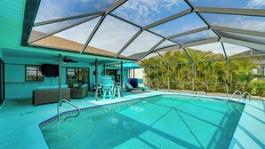 A swimming pool with a covered area, lounge chairs, and a view of palm trees. - Family Fun in Cape Coral! Colorful Home w/ Dock (Cape Coral)