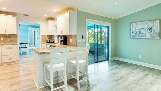A modern kitchen with white cabinets, granite countertops, and a breakfast bar with white chairs. - Family Fun in Cape Coral! Colorful Home w/ Dock (Cape Coral)
