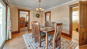Une salle à manger avec une table en bois, six chaises, un lustre et un tapis à motifs floraux.