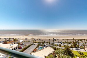 A beachside view with a parking lot, a pool area, and a building with a flat roof. - San Luis Resort Condo with ocean view, balconies, shared hot tub & pool, WIFI (Galveston)