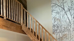 Un escalier en bois menant à l’ étage supérieur, une petite cuisine équipée d’un réfrigérateur, une chaise et une porte blanche.