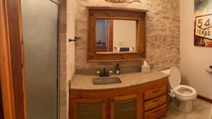 Ein Badezimmer mit Steinwand, Holzwaschtisch, Waschbecken und Toilette.