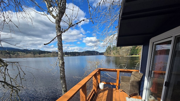 Une terrasse en bois avec une balustrade donnant sur un lac, une chaise en osier et une porte menant à un espace abrité.