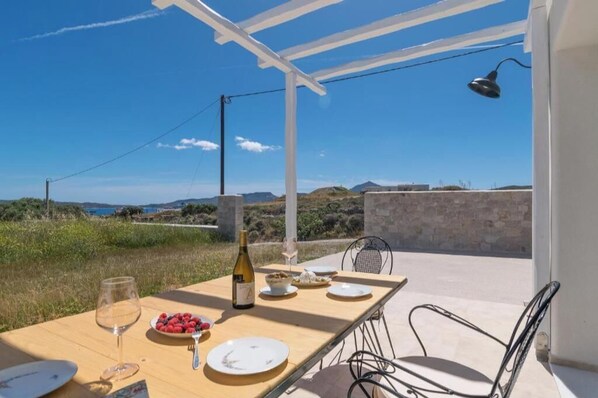 Un espace de restauration en plein air avec une table dressée pour deux personnes, une bouteille de vin et un verre d’eau.