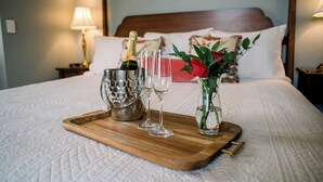 Una bandeja de desayuno ordenada sobre la cama, con una botella de champán, dos copas y un florero con una rosa roja.