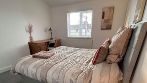 Et soveværelse med en seng, et sengebord med lampe, et vindue og en radiator.