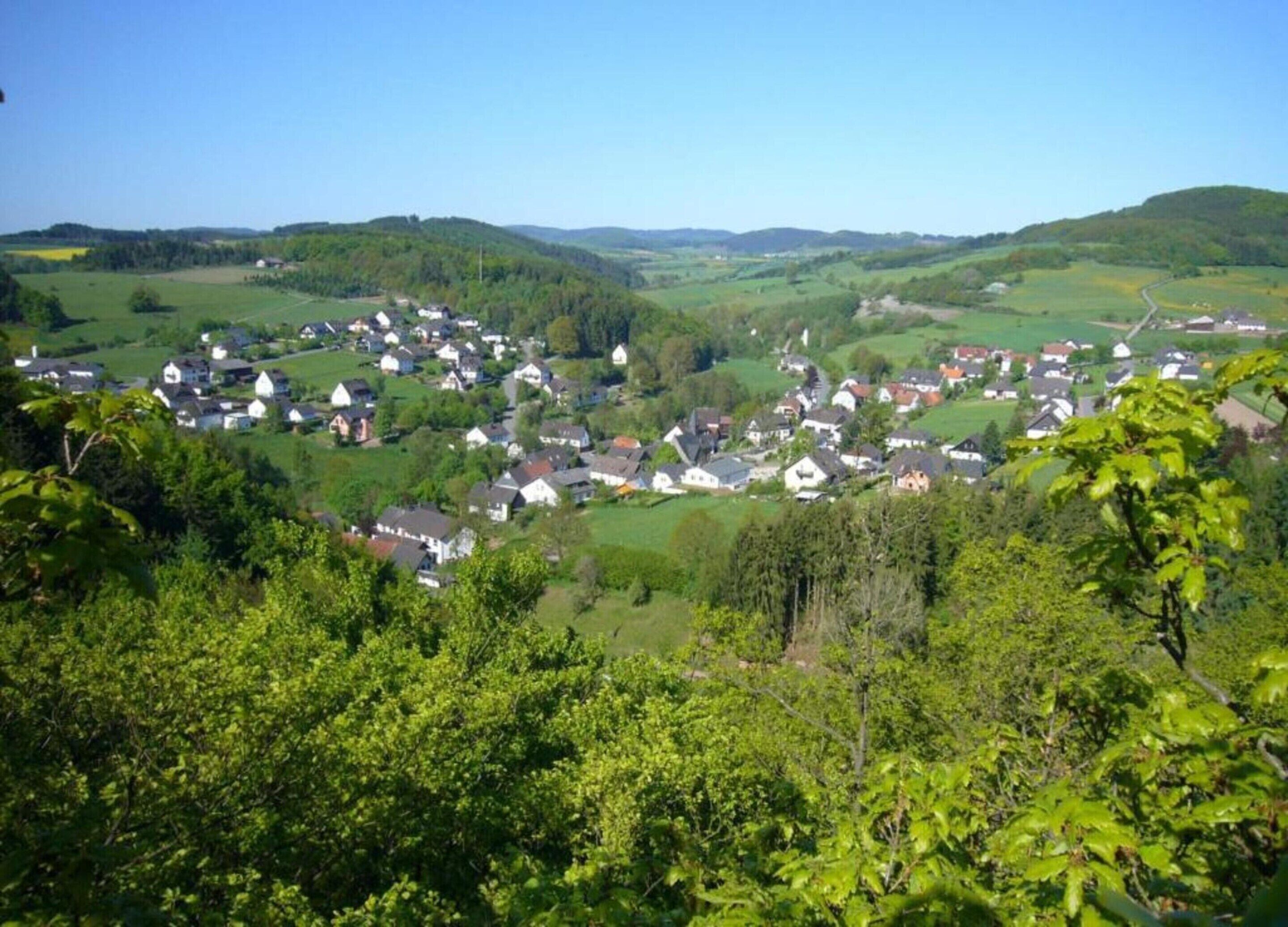 A rural village with houses surrounded by lush greenery and rolling hills.