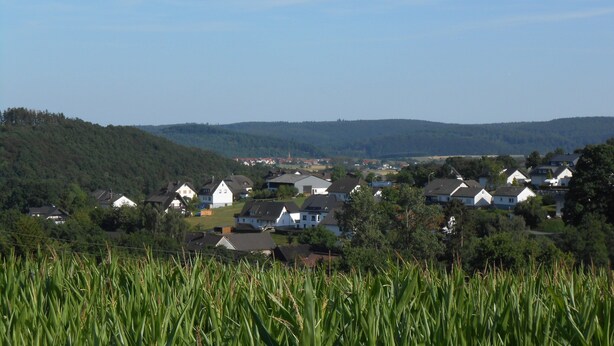 Uma aldeia rural com casas rodeada por campos e colinas.