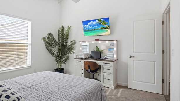 Et soveværelse med en seng, et skrivebord med computer, en plante og et TV på væggen.