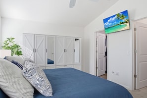 Ein Schlafzimmer mit einem Bett, einem Kleiderschrank, einem Fernseher und einer Pflanze.