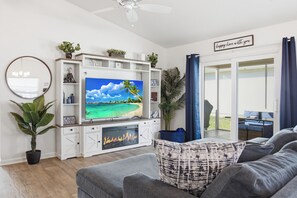 A living room with a flat-screen TV, a fireplace, a sofa, and a view of the outdoors. - The Villages Rental - Golf Cart - Fenced Yard - Large Dogs - Brownwood (The Villages)