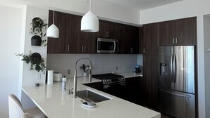 Eine moderne Küche mit dunklen Holzausziehtüren, Edelstahlgeräten und einer weißen Kochinsel mit Barhocker.