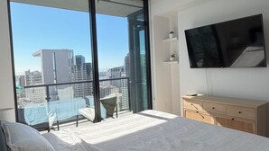 Ein Schlafzimmer mit einem großen Bett, einem Fernseher, einem Schminktisch und einem Balkon mit Blick auf die Stadt.