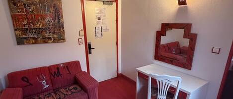 Une pièce avec un canapé rouge, une table blanche, un bureau blanc et un luminaire fixé au mur.