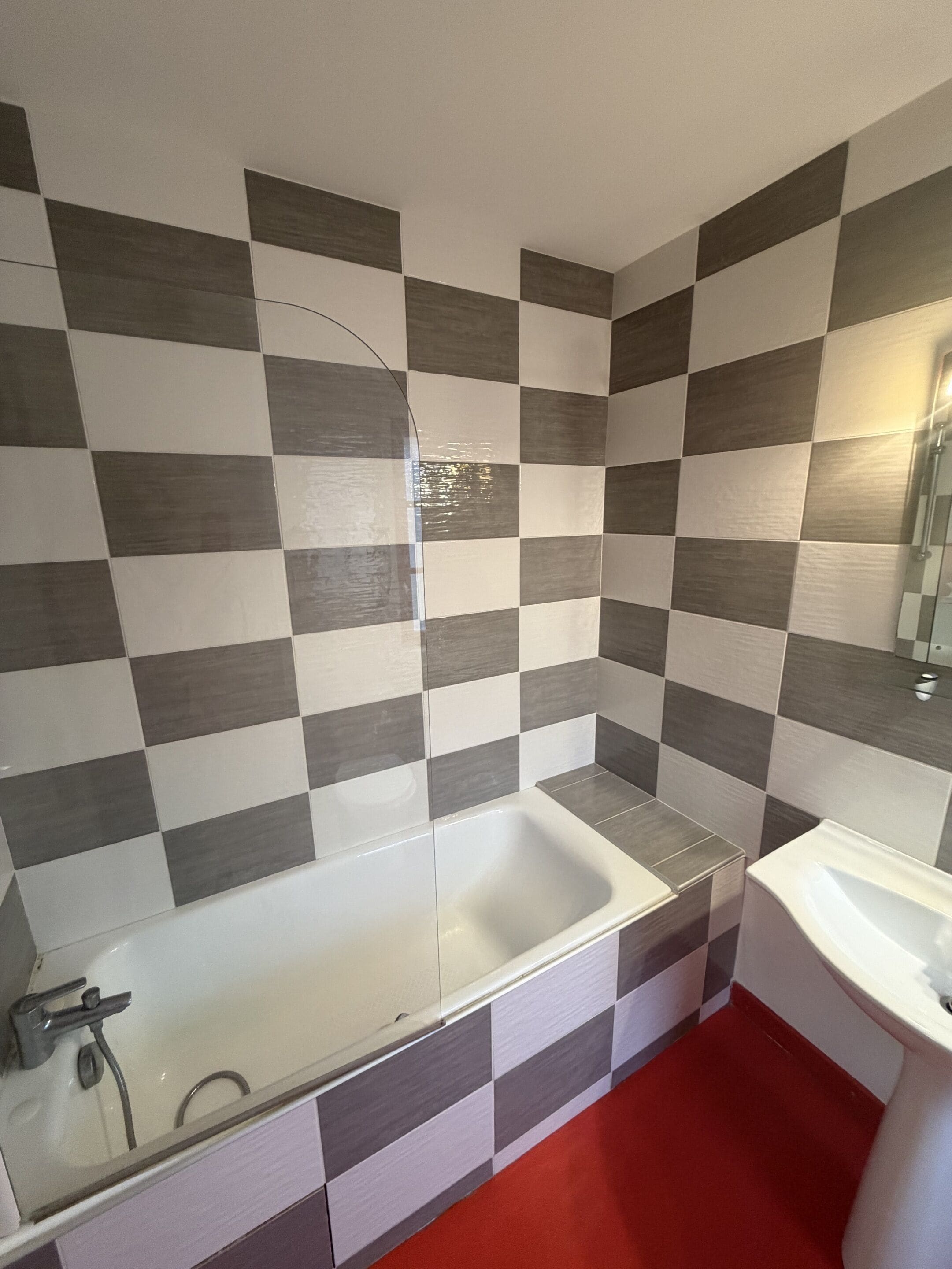 A bathroom with a checkered tile wall, a bathtub, and a sink.