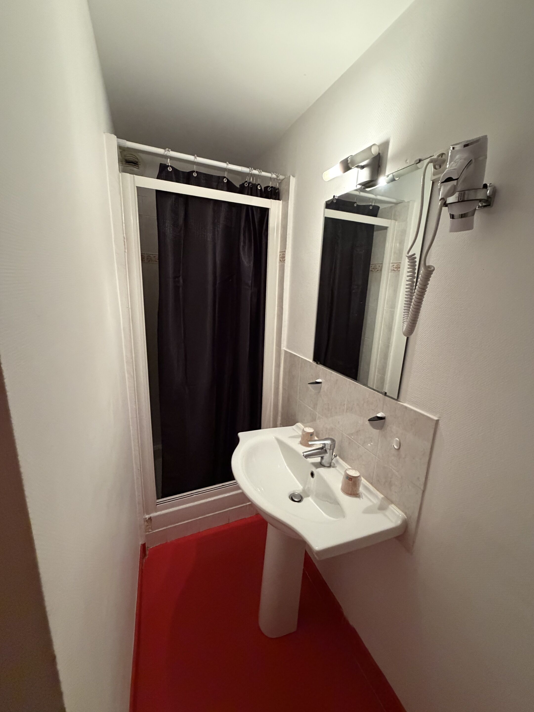 Un bagno con un lavandino bianco, uno specchio, una tenda da doccia e un tappeto rosso.