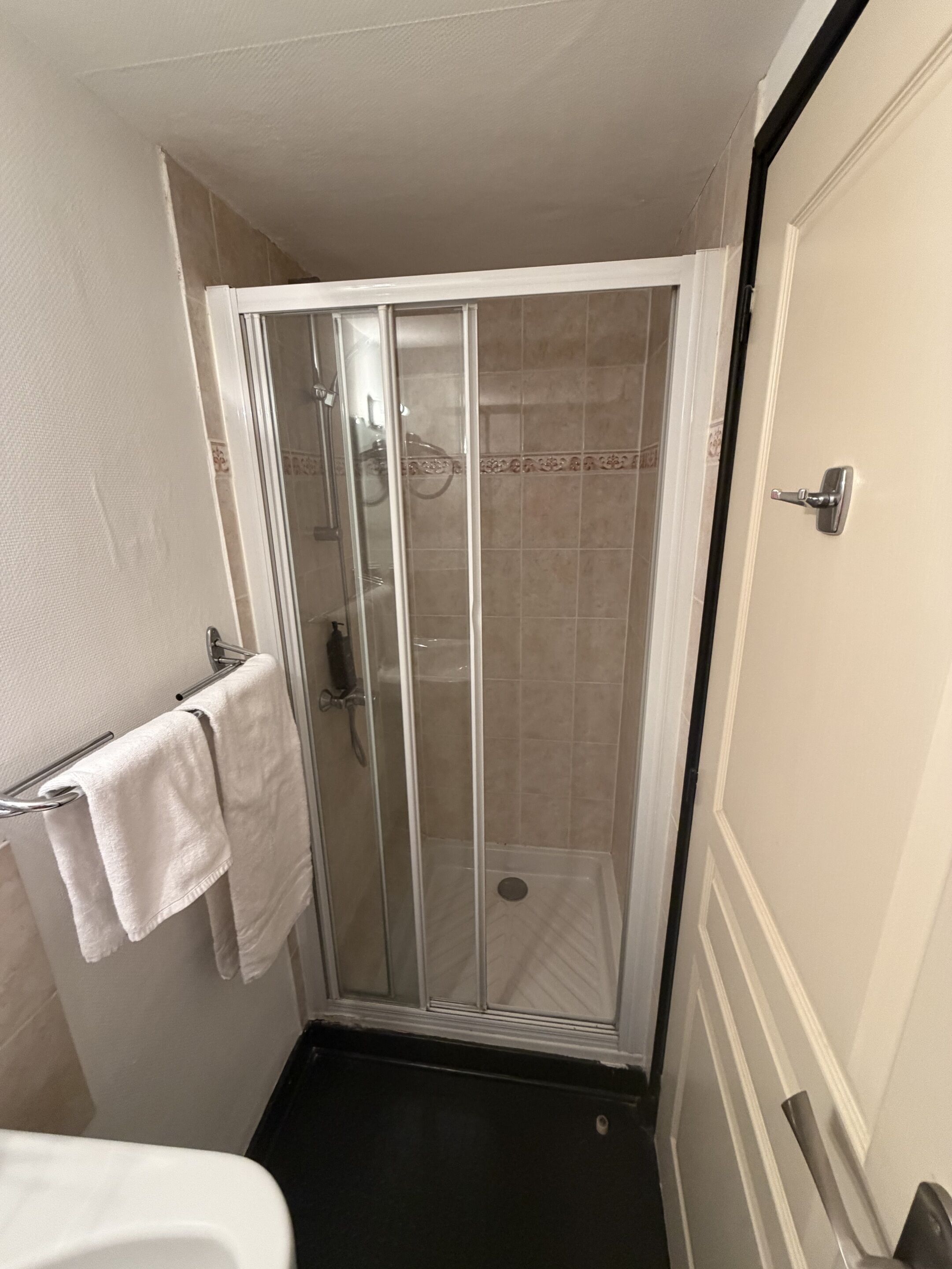 A small, enclosed shower area with a glass door, a towel rack with a white towel, and a door with a silver handle.
