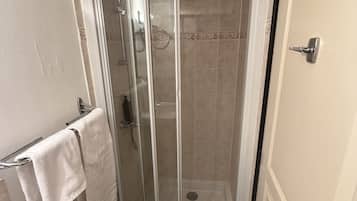 A small, enclosed shower area with a glass door, a towel rack with a white towel, and a door with a silver handle.