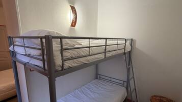 A bunk bed in a room with a small stool and a wall-mounted light fixture.