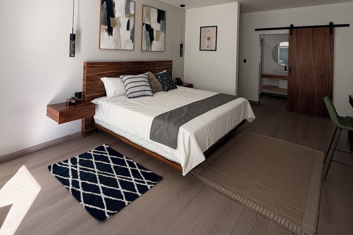 Un dormitorio moderno con una cama grande, una mesita de noche de madera, una lámpara colgante, arte abstracto en la pared y un armario con puertas correderas.