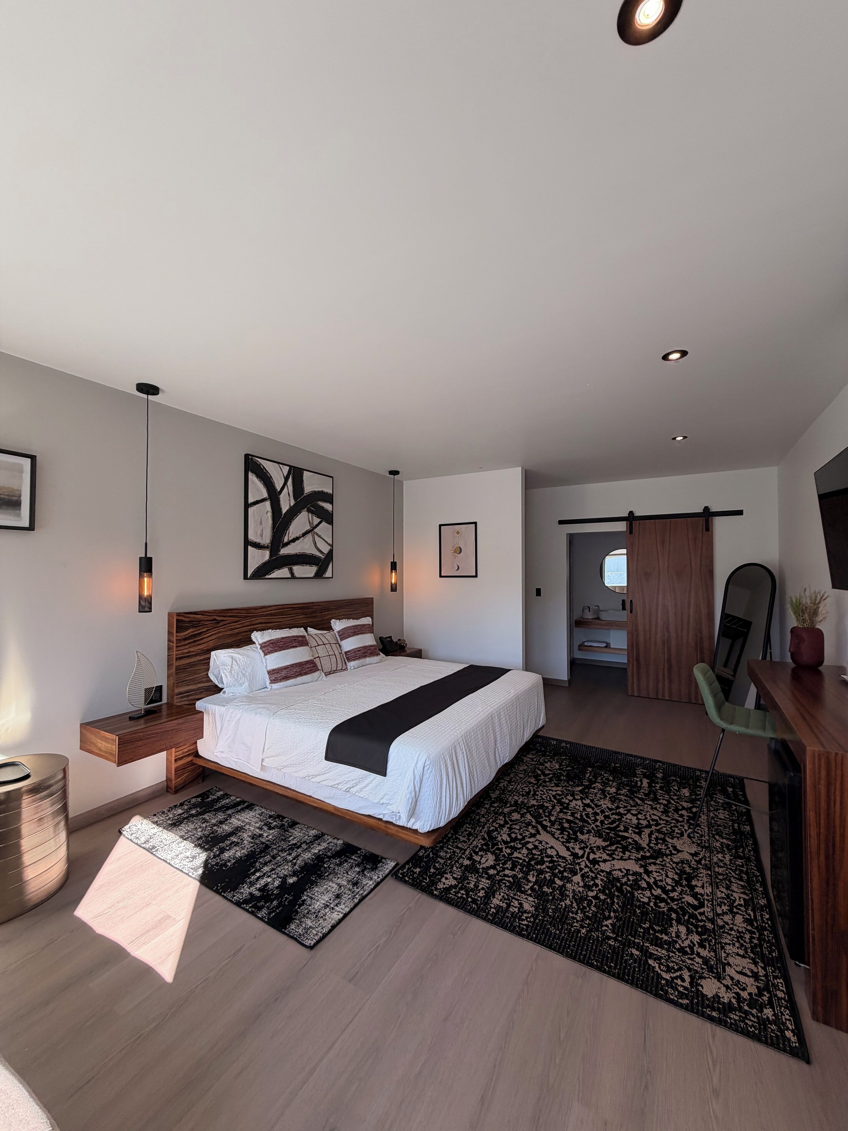 A modern bedroom with a large bed, bedside tables, a desk, and a mirror.