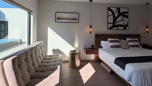 Egy modern hálószoba, amelyben egy nagy ágy, egy kanapé, egy dohányzóasztal és egy kép található a falon.