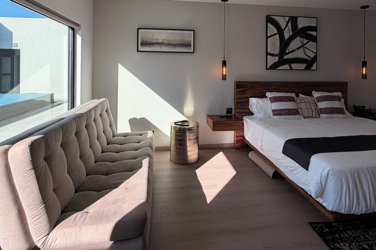 Un dormitorio moderno con una cama grande, un sofá, una mesita de noche y un cuadro en la pared.