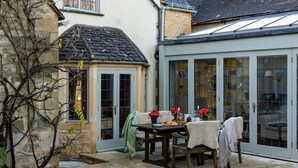 Ein gemütlicher Patio-Bereich mit Esstisch, ein kleiner Garten und ein Wintergarten mit Glastüren.