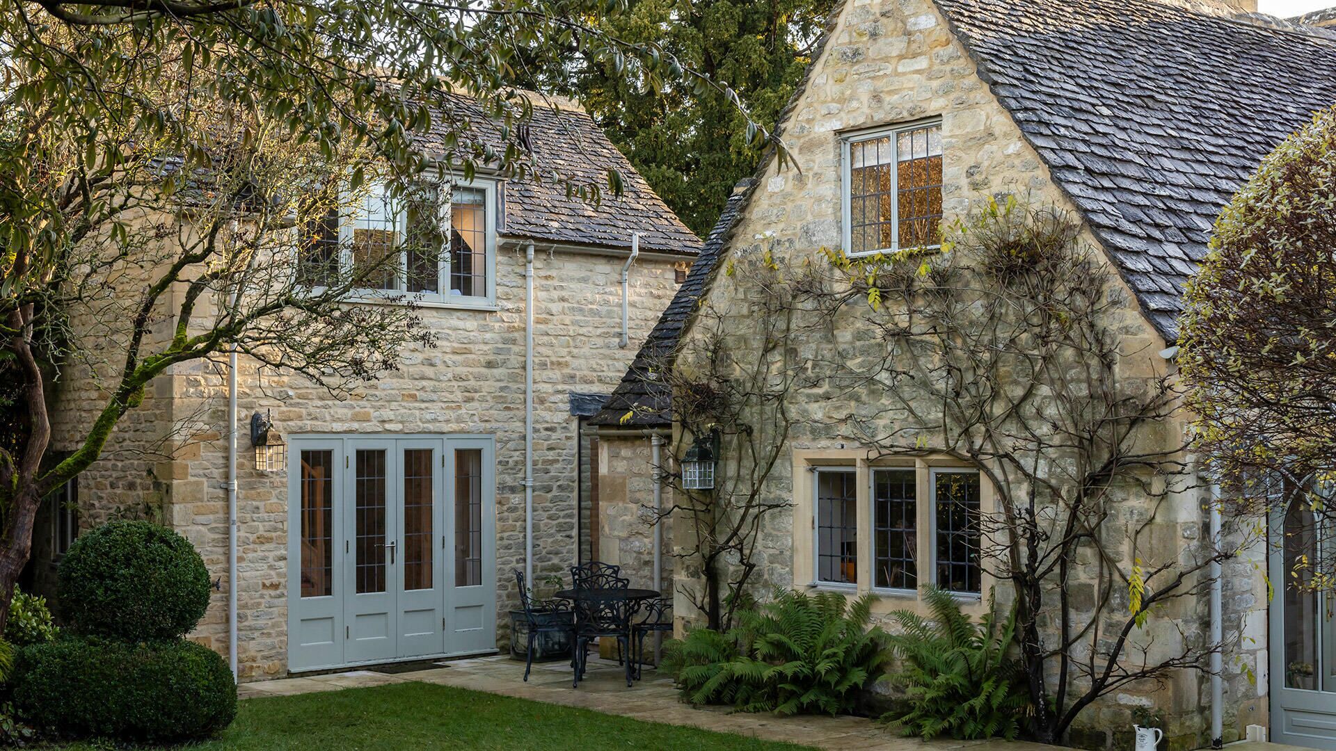 A stone house with a tiled roof, a front door, and a small patio with a table and chairs.