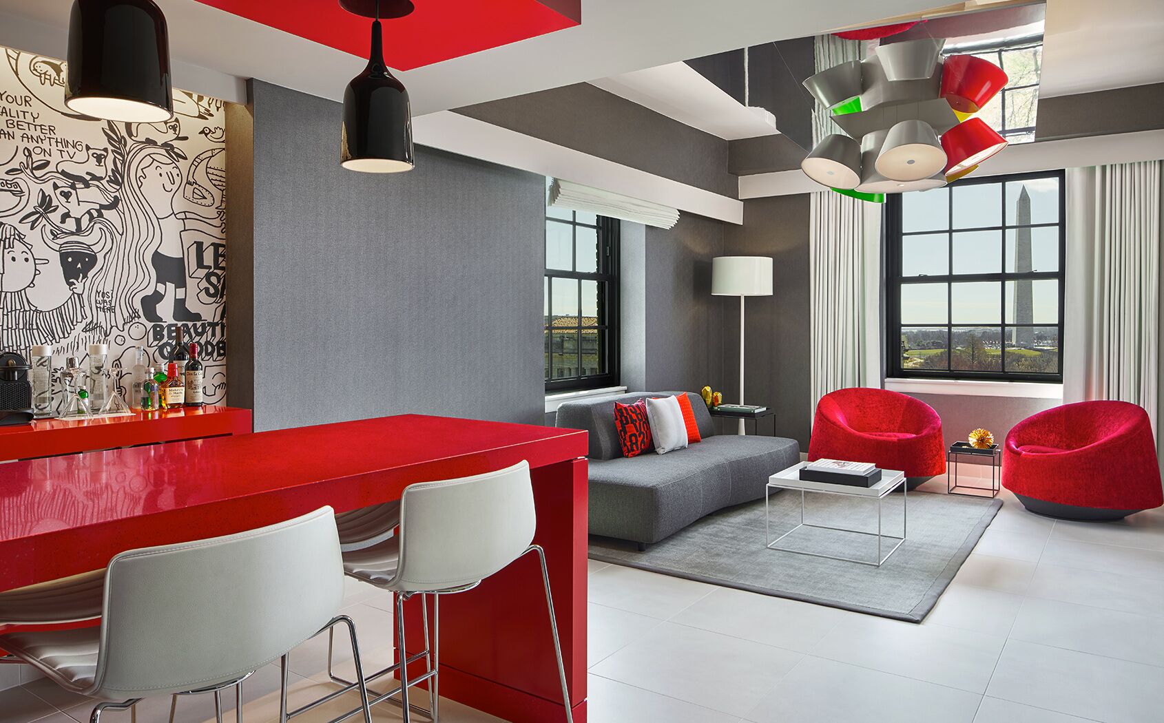 Una sala de estar moderna con una barra roja, un sofá gris y sillas rojas.