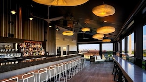 Un bar moderne doté d’un long comptoir, de nombreux tabourets et offrant une vue sur le paysage urbain grâce à de grandes fenêtres.