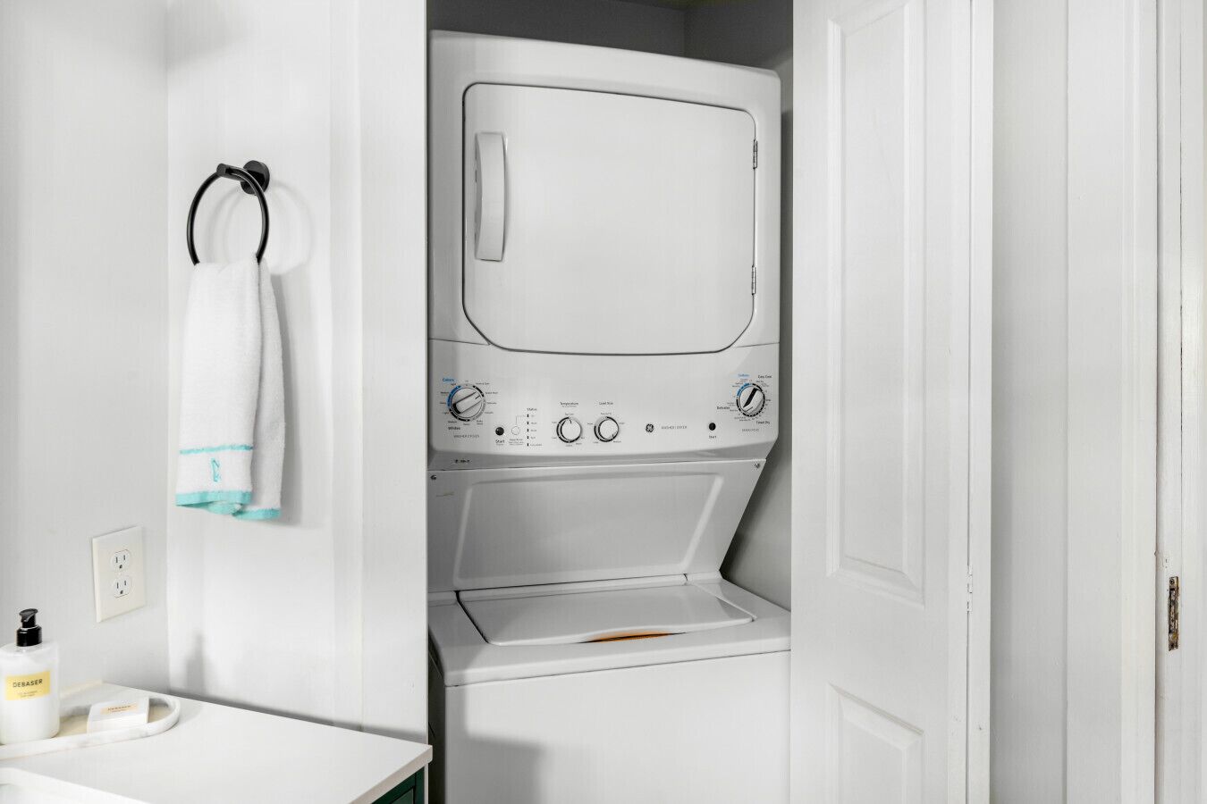 A compact laundry room with a built-in washer and dryer, a towel rack, and a sink with a bottle of hand soap.