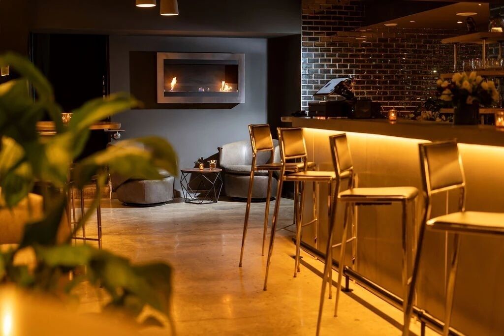 A bar area with a modern design, featuring a brick wall, a flat-screen TV, and a seating arrangement with bar stools.