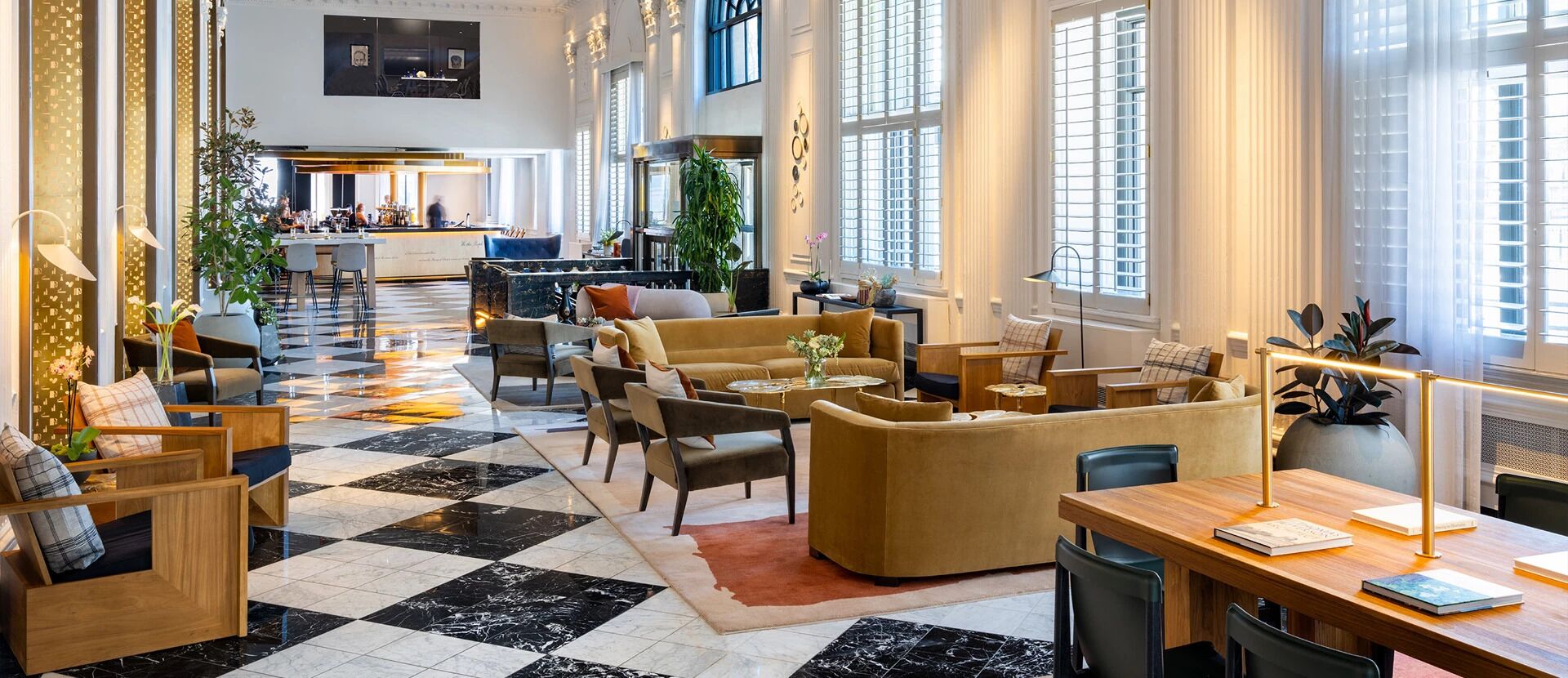 Un hall d’hôtel spacieux, doté d’un sol à carreaux, de coins salon, d’un bar et de grandes fenêtres.