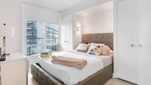Ein modernes Schlafzimmer mit Bett, Nachttisch und Fenster mit Blick auf die Stadt.