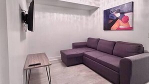 Ein modernes Wohnzimmer mit einem Ecksofa, einem kleinen Holztisch und einem an der Wand montierten Fernseher.