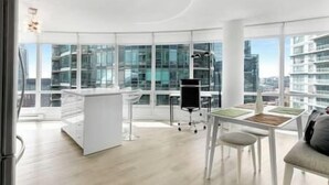 Ein moderner, offener Arbeitsbereich mit großem Fensterblick auf eine Stadtlandschaft, einem weißen Schreibtisch, einem schwarzen Stuhl und einem weißen Sofa.