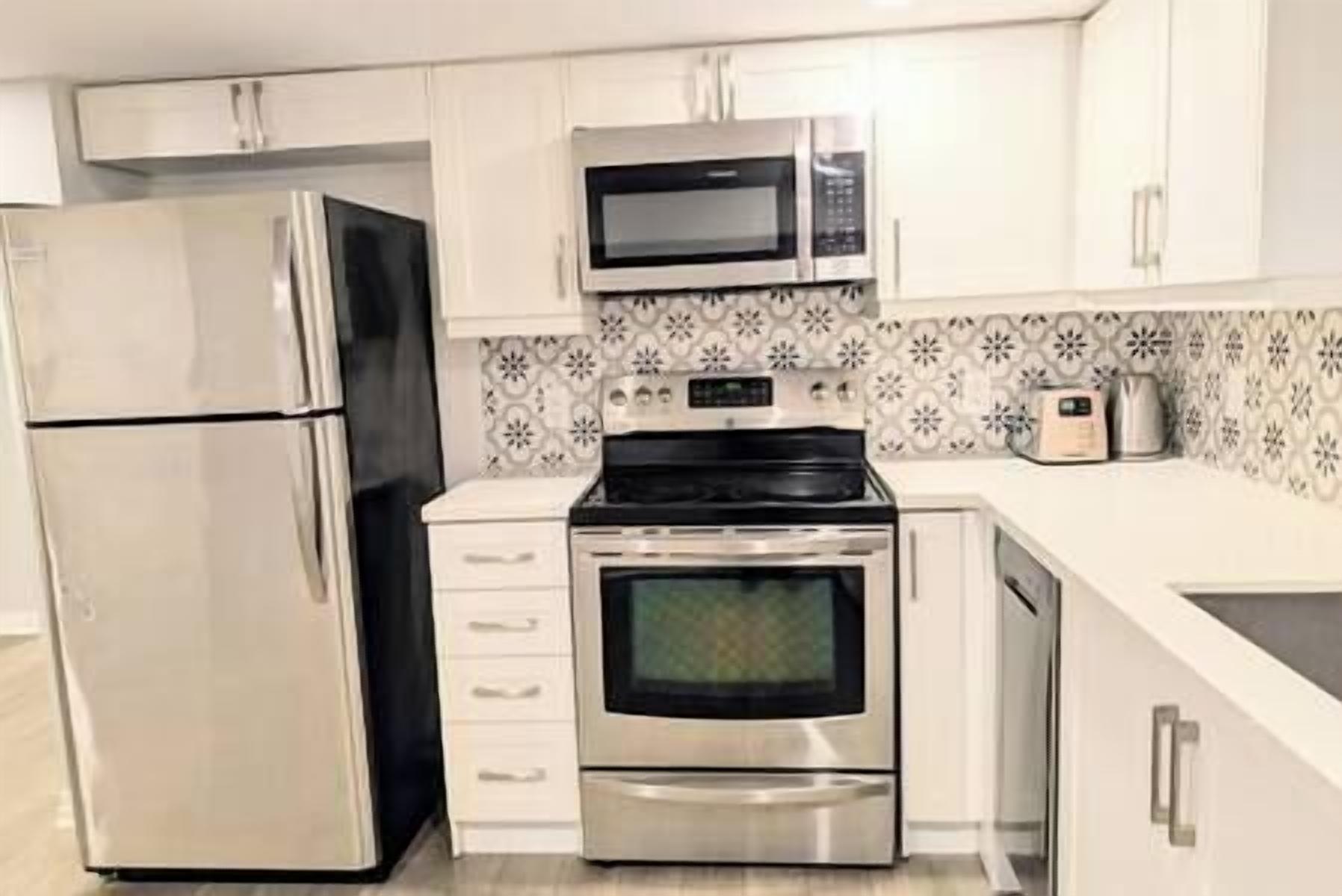 A kitchen with stainless steel appliances, white cabinets, and patterned backsplash.