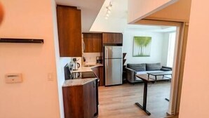 A modern kitchen with wooden cabinets, a refrigerator, and a coffee maker. There is a dining area with a table and chairs.