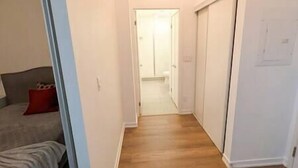 A narrow hallway with wooden flooring, a red pillow on a couch, and a white door at the end.